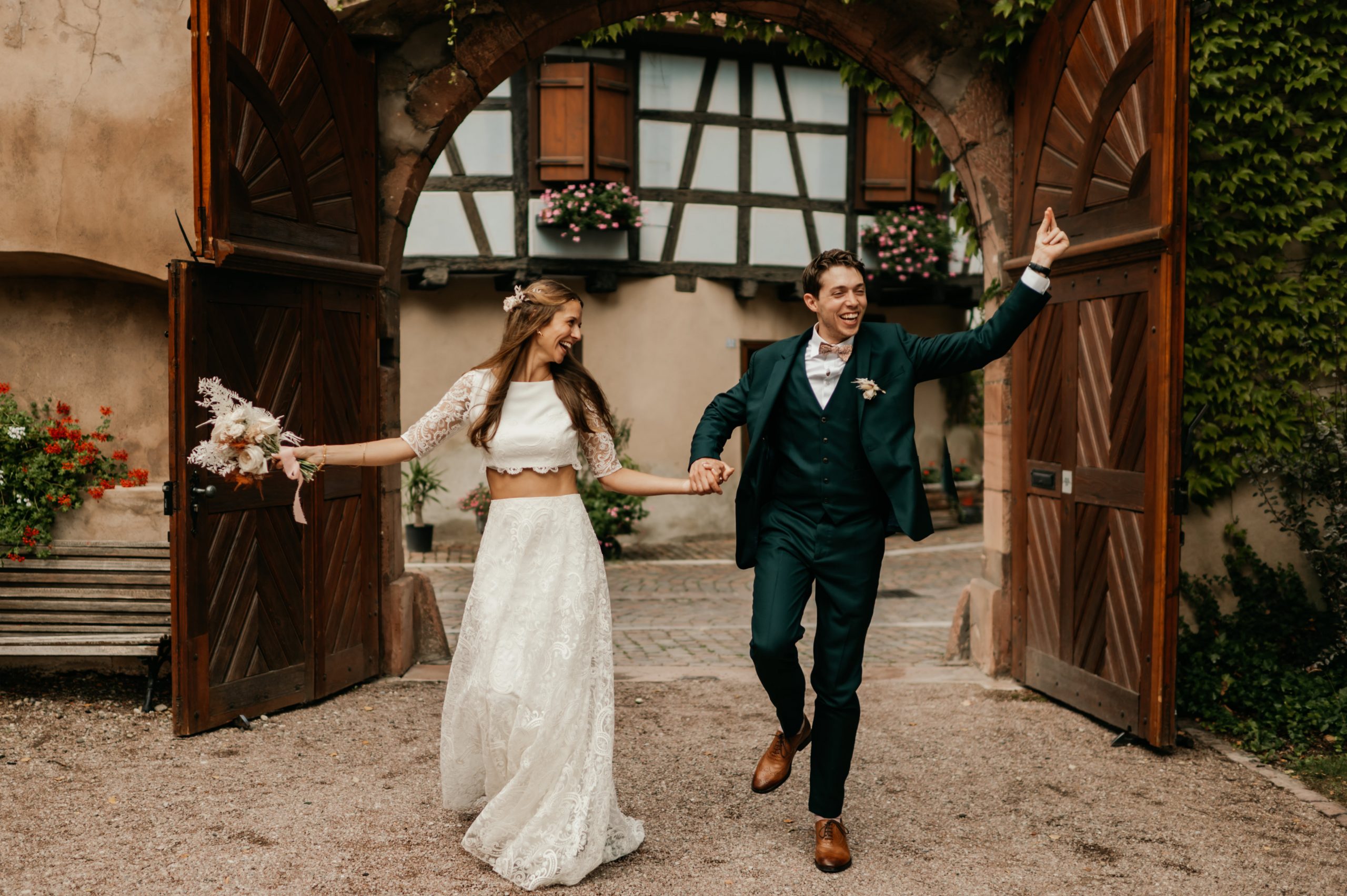 Sam et Laure faisant leur entrée dans la cour d'une maison alsacienne, photo de mariage par Pauline Kupper, photographe Alsace